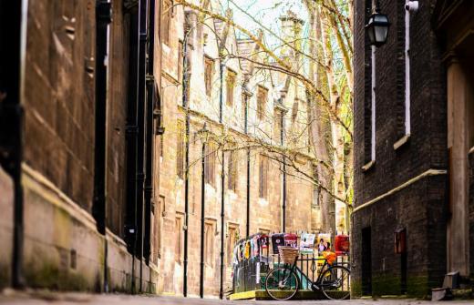 Meet Cambridge - looking through an old brick arch at ground level where there is a black framed bicycle with a wicker basket leaning against black iron railings