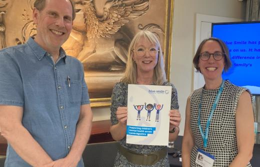 Group picture of Simon Baron-Cohen, Amanda Langford and Anne Kent-Taylor, smiling and holding a Blue Smile folder