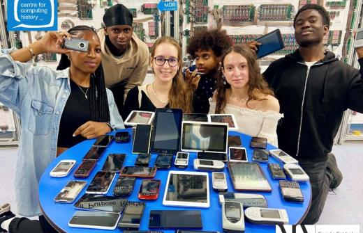 A group of young people at the Centre for Computing History, behind a table of old mobile phones and tablets ready for recycling