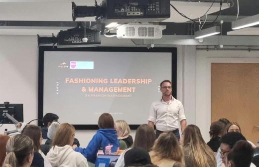 Nick is stood in front of an audience of students with a screen and introduction slide behind him.