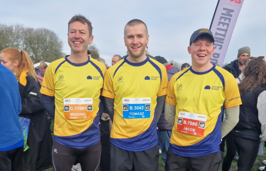 Three runners in Cambridgeshire Community Foundation branded yellow and navy running tops standing in a crowd of runners.