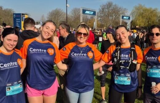 A group of five people standing together outdoors at Cambridge Half Marathon 2025 event, smiling at the camera. They are wearing matching blue and orange "Centre 33" shirts