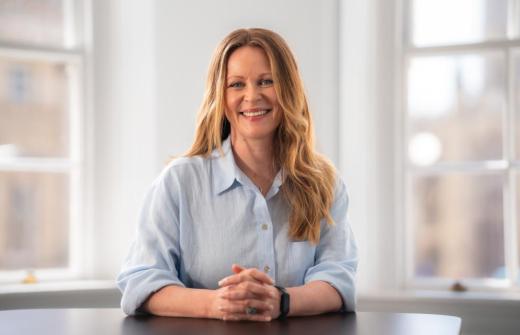 Deborah Fleming smiling at the camera, sitting down, hands clasped in front of her.