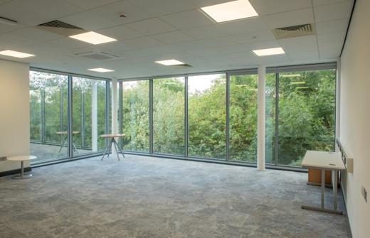 A large office with floor to ceiling windows, overlooking trees