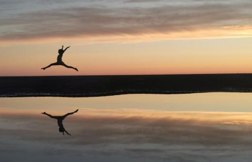 Girl leaping across the sand at sunset