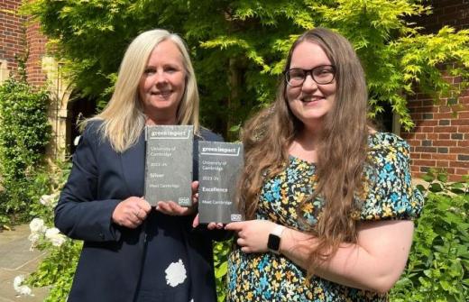 x2 white women standing in a lush green garden holding a grey slate award for Green Impact