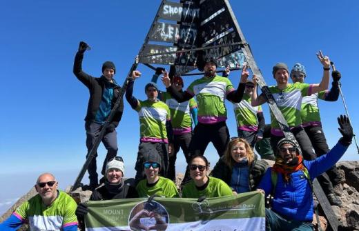 Group of men and women dressed in green at the top of a mountain with a sign 