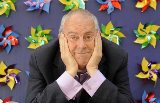 Gyles Brandreth resting his face in his hands. Purple background with windmills on it. 
