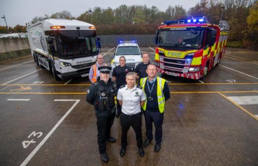 Three people stood in front of a bin lorry, police car and fire engine