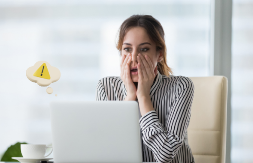 A woman looking shocked as she looks at her laptop screen implying she's made a big mistake