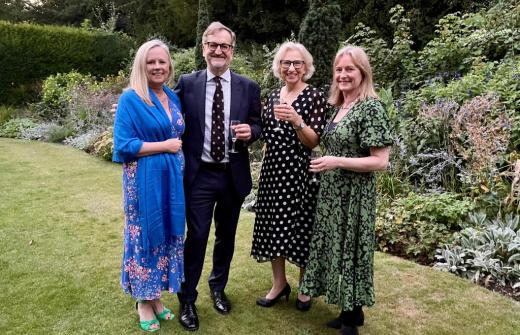 3 white woman and 1 white mean standing in a College garden smiling at the camera with drinks in their hands