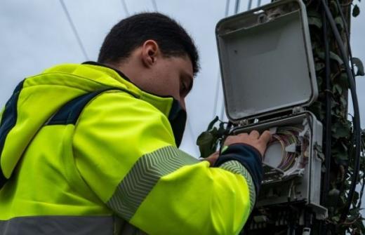 Telecom field engineer in a high-visibility jacket working on a box with cables in it