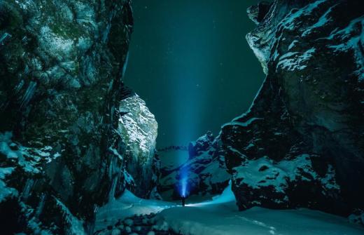 A figure with a torch in a dark, snowy ravine.