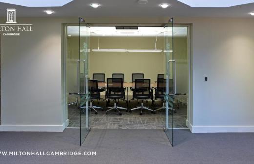 Photo shows glass doors open on a room set up for a meeting with chairs around a rectangular table. 
