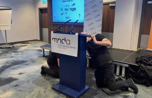 Two men moving a lectern at the front of a conference hall