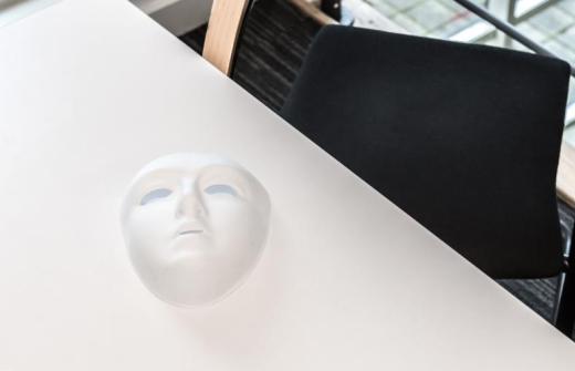 White mask on a white table with dark chair in the background