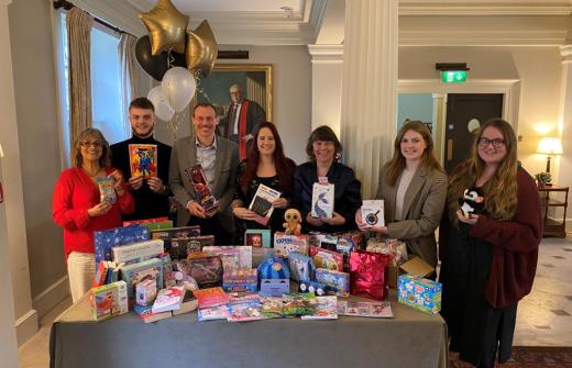 A mix of men & women smiling into the camera holding toys behind a table laden with toys