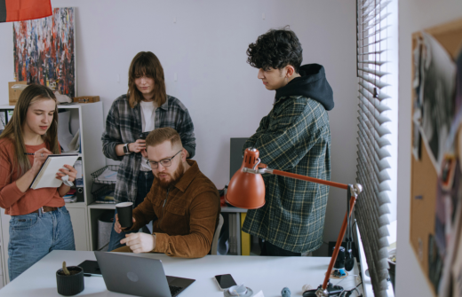 A group of young people chatting to each other around a person working at a laptop