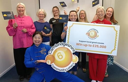 Charity representatives standing together holding signs with the Cambridgeshire Community Lottery logo and a branded lottery ticket.