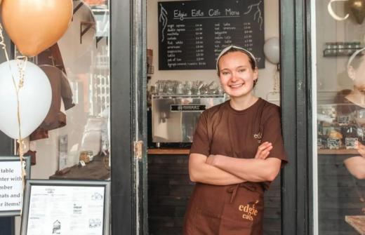 Woman leaning on the door frame of her cafe, smiling at the camera.