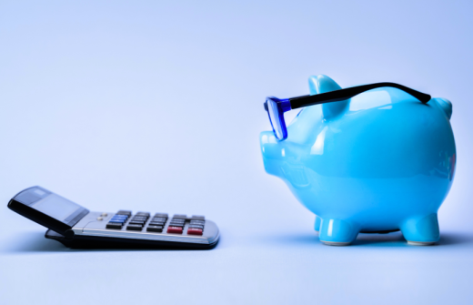 A blue piggy bank with glasses looking at a calculator