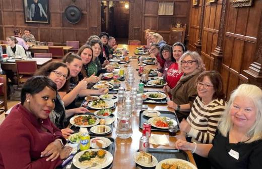 A mixed group of people eating at a long wooden table in a Cambridge College