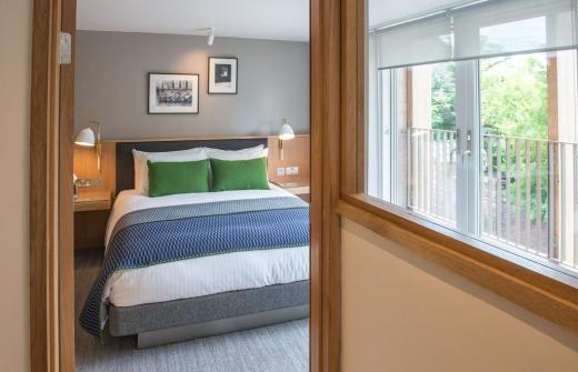 An award winning en suite bedroom at Jesus College Cambridge, West Court. The room has large windows and the room is light, bright & airy. There is a double bed in the middle with white linen & emerald scatter cushions