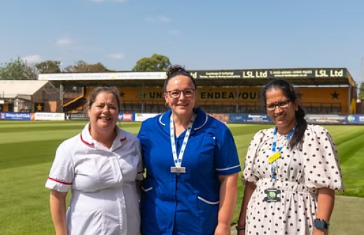 three nurses stand, smiling, in front of the cledara abbey stadium on a sunny day 
