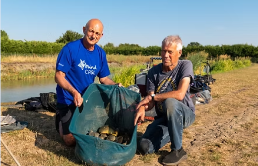 two men, including ian darler, left, kneel proudly beside a large net full of fish