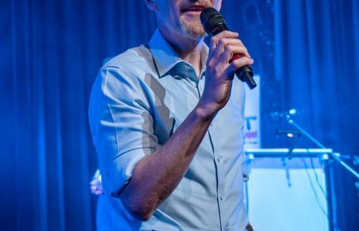 A bald man standing and speaking while holding a microphone.