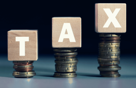 Letter blocks spelling out TAX balancing on stacks of coins