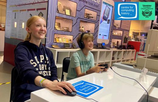Smiling children explore an interactive exhibit at the Centre for Computing History. The centre's logo is displayed with the Traveller's Choice Award logo in the top right corner