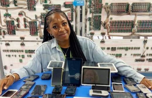 Smiling young woman with a table of outdated technology including mobile phones and tablets