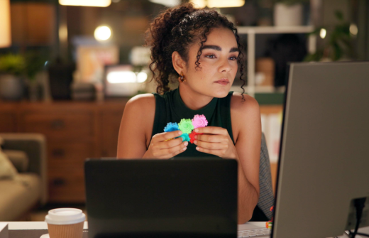 Remote worker - a female with a black tank top sits at their desk with a laptop open. They are staring at a computer screen and are playing with a fidget toy.