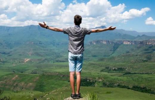 Young man standing on mountaintop with arms open wide across countryside view