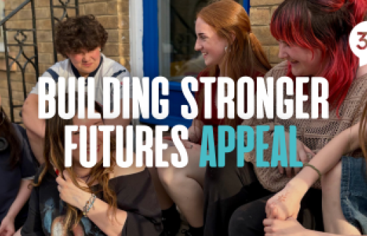 A group of young people sitting on the steps of the new Centre 33 building, laughing and smiling, with the text "Building Stronger Futures Appeal" over the top