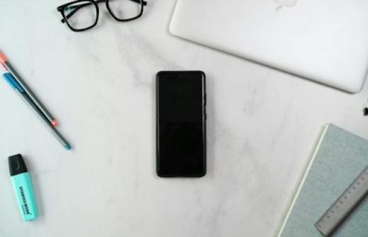  A phone, laptop and notebook on a desk. 