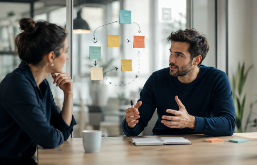 Two people discussing a changing role beside a flexible workflow map, representing how startups interview for adaptability, judgement and future contribution.