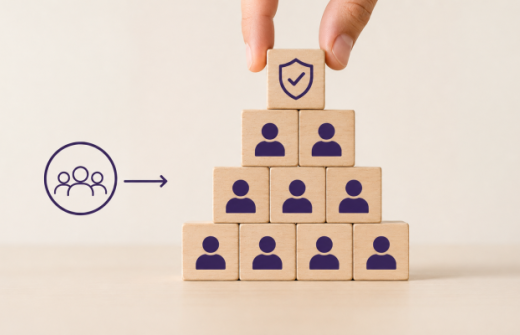 Hand placing a structured block onto a team pyramid, representing how growing companies protect culture by turning values into repeatable hiring processes.