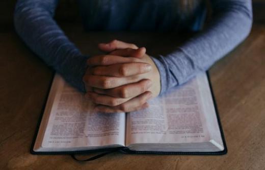 man with hands together over an open book
