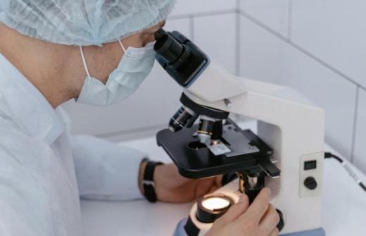 Scientist looking down through a microscope and reviewing data on a chart. 