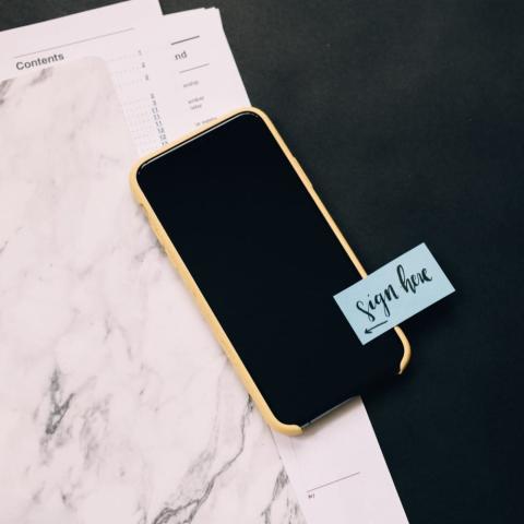 A mobile phone with a written note on it saying sign here.