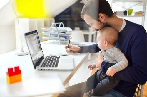 man working from home while holding a baby
