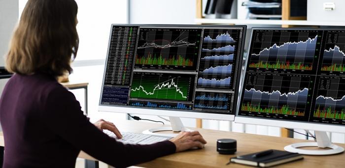Trader working with two screens showing trading graphs