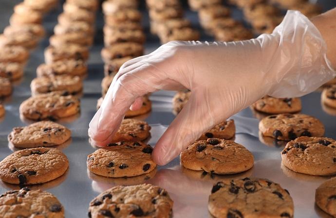 Image shows a production worker checking biscuit quality on a production line