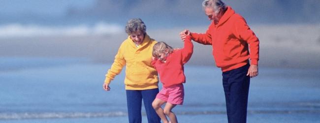 Grandparents hold child's hands and lift her up while walking on beach