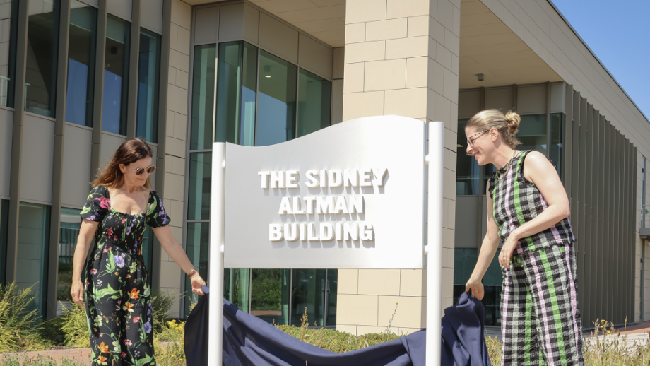2 ladies in front of a sign the Sidney Altman Building at the Babraham Research Campus