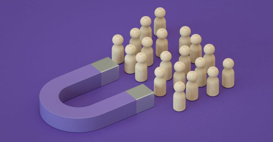 A magnet on a purple background attracts a group of wooden pins