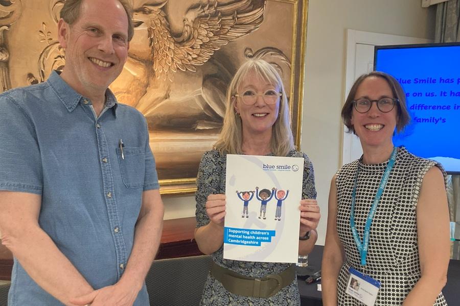 Group picture of Simon Baron-Cohen, Amanda Langford and Anne Kent-Taylor, smiling and holding a Blue Smile folder