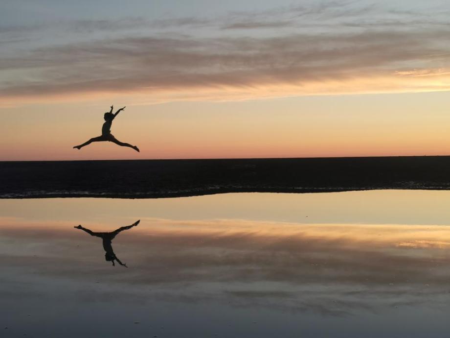 Girl leaping across the sand at sunset